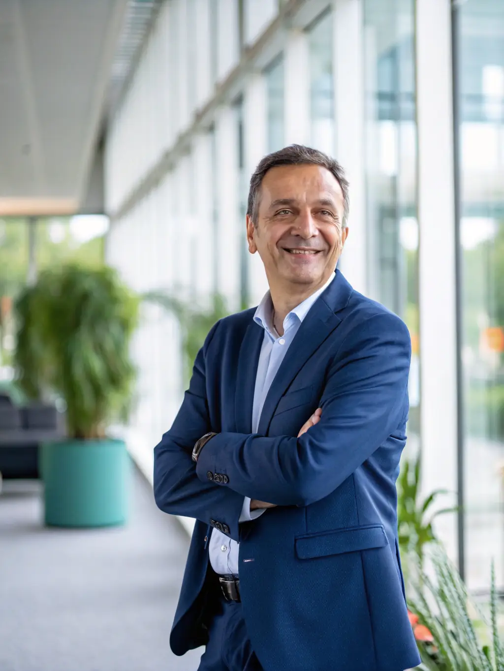 A professional coach in a suit, smiling confidently while gesturing towards a whiteboard filled with strategic business plans, set in a modern office in London.